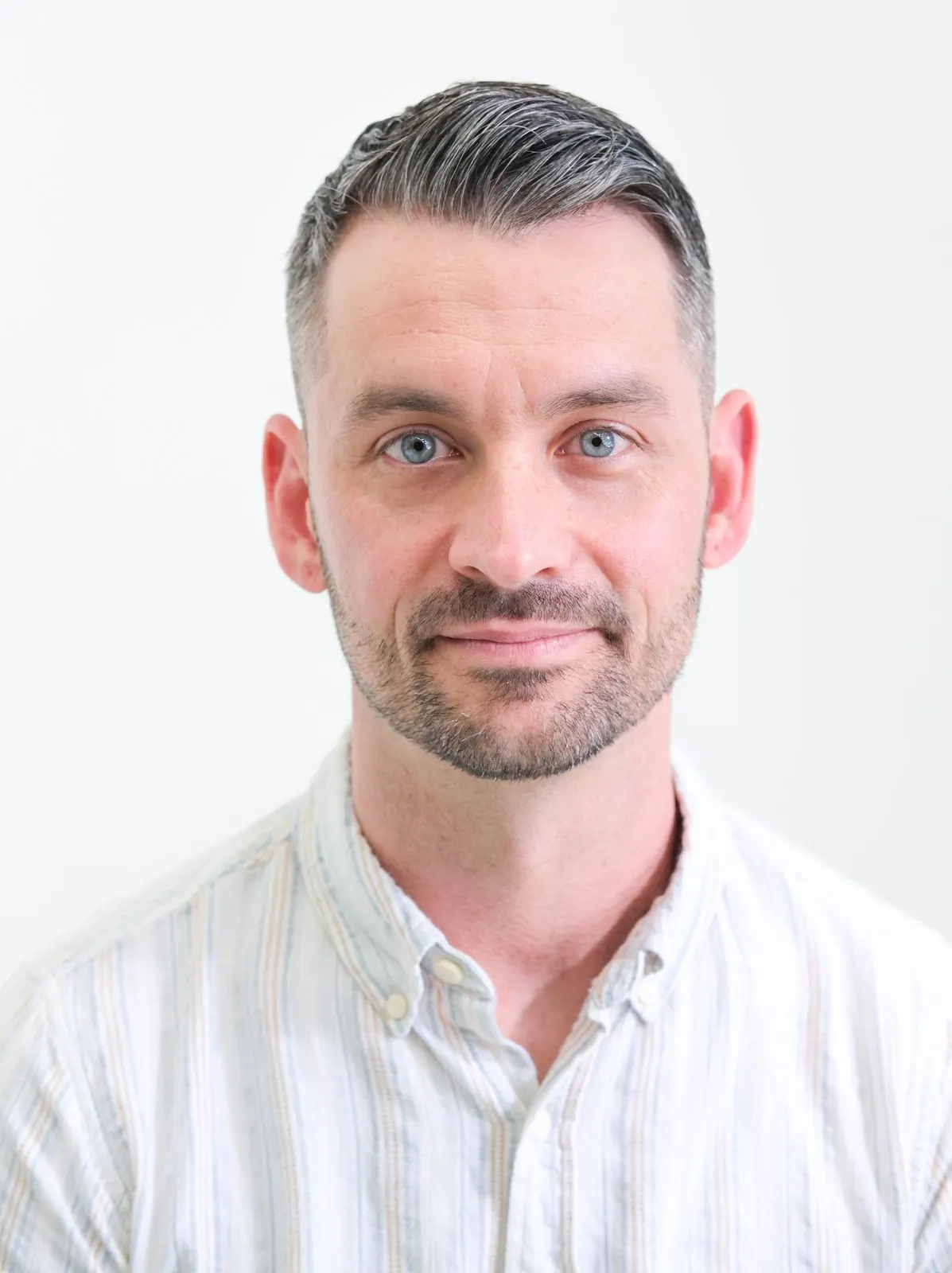 Professional studio headshot of a man in a light button-down shirt, looking directly at the camera